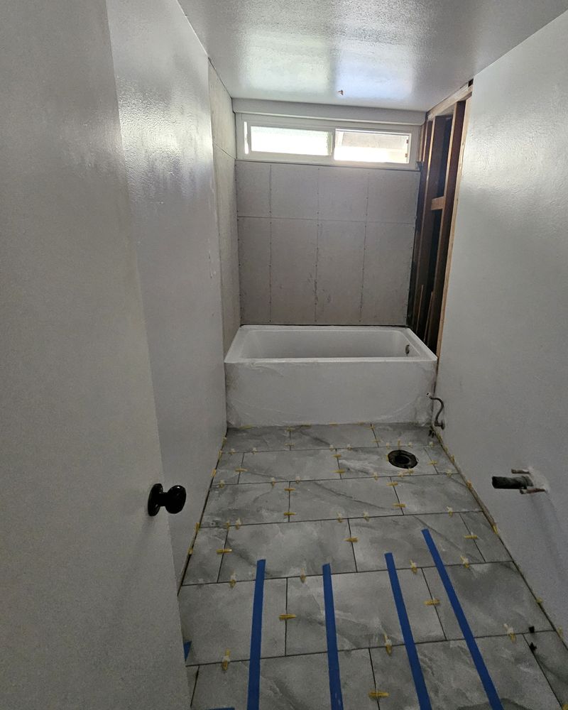 The same hall bathroom with a new tub set, backer board on the tub walls, and floor tile going down with leveling clips