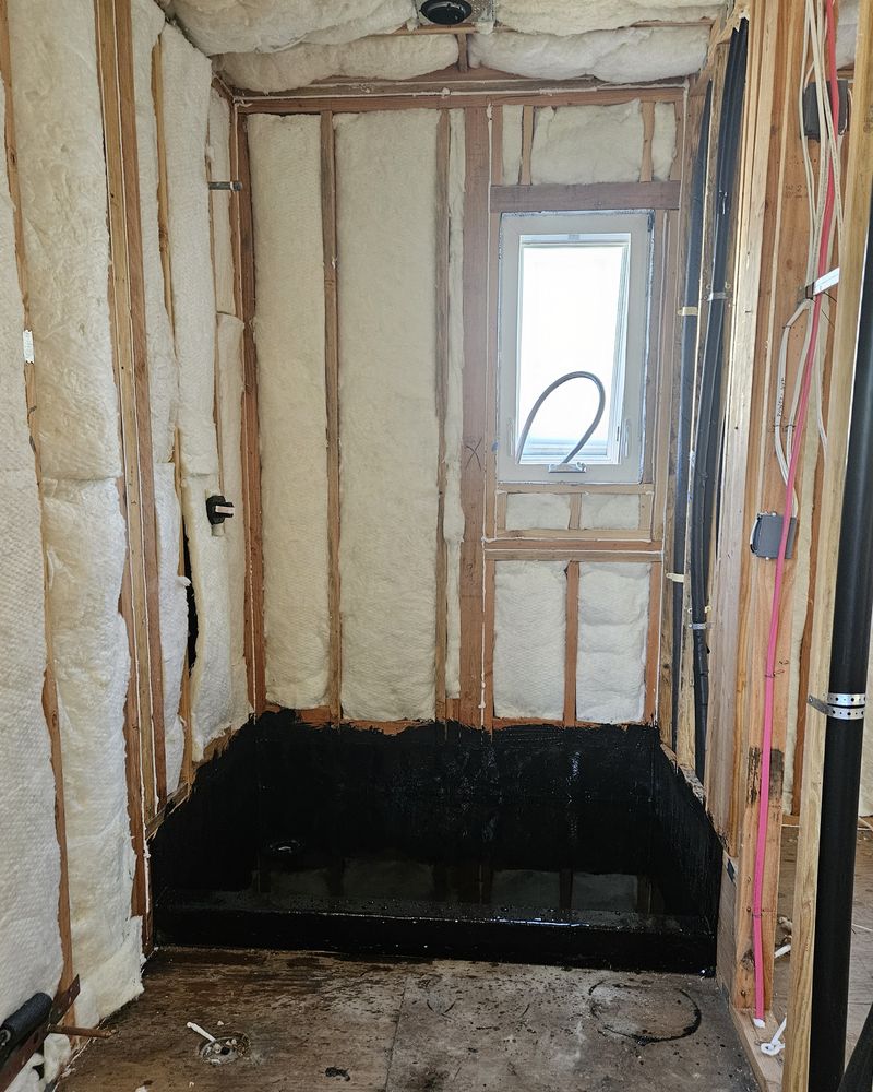 Shower bay as open framing with insulation, a window, and a black waterproofed base