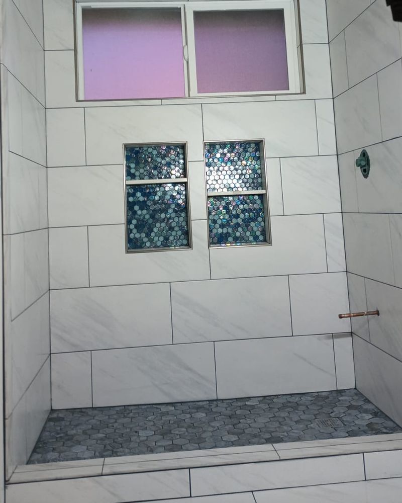 The same shower with large white wall tile, two glass mosaic niches, and a hex mosaic floor