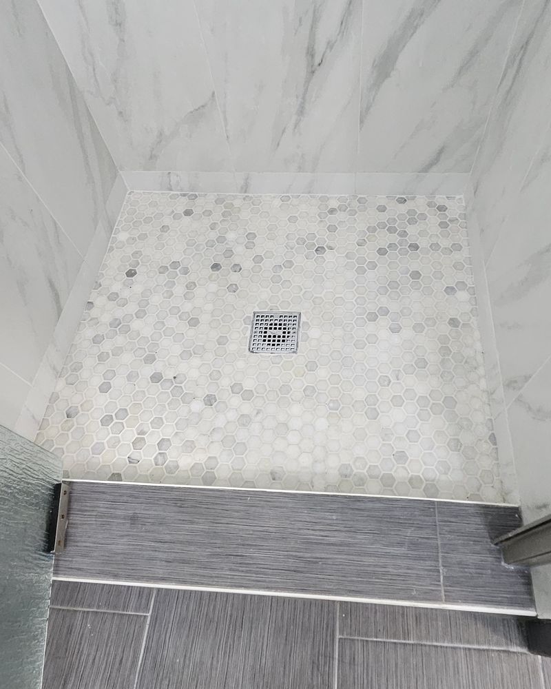 The same shower stall with a new white and gray hex mosaic floor and a square drain