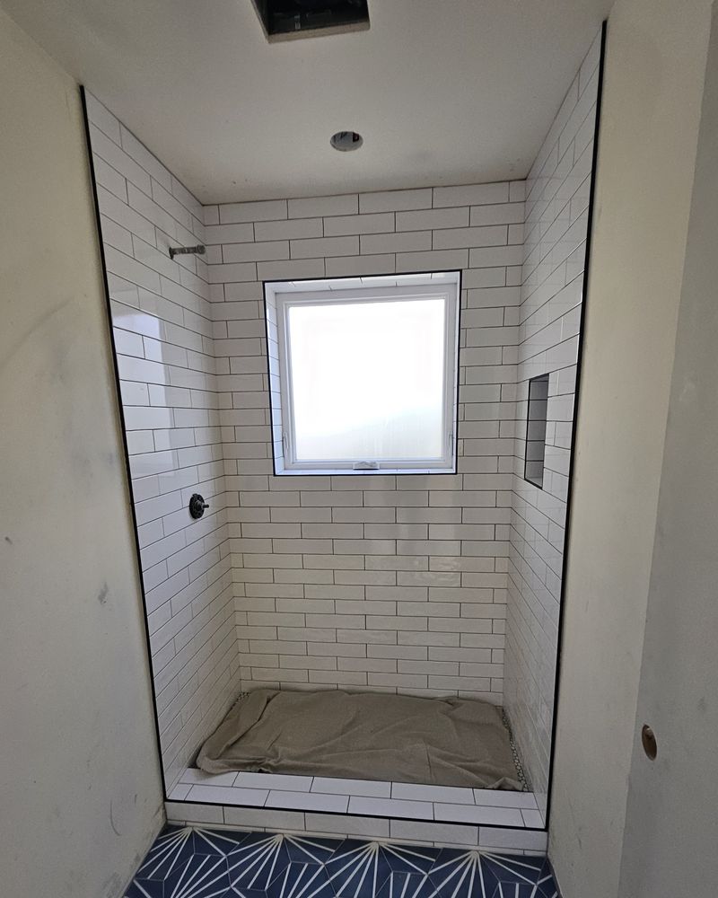 The same bathroom with the shower tiled in white subway tile and a blue patterned floor