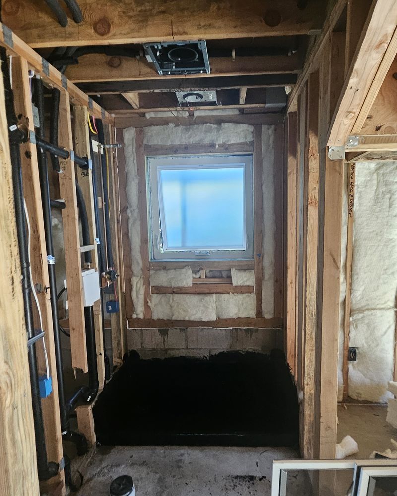 Bathroom as open framing with exposed pipes and wiring and a window in the shower bay