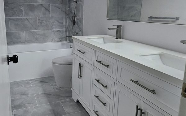 Hall bathroom with a white double vanity, two undermount sinks, and a tub surround and floor in gray marble look tile