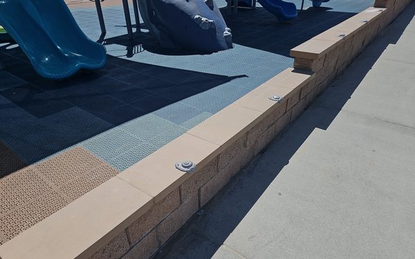 Precast concrete caps running along the top of a block wall, bolted down through the cap