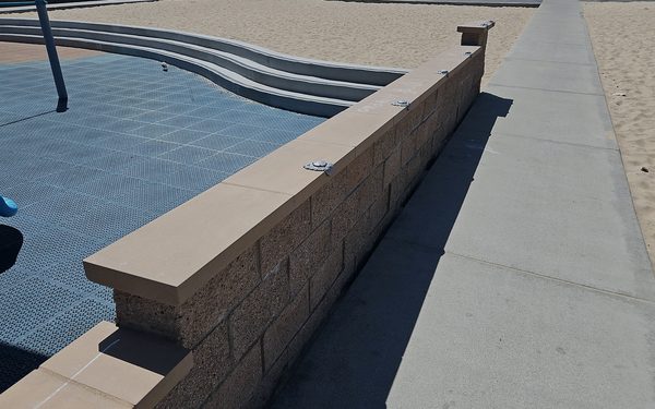 New precast concrete caps set along a low block wall beside a playground surface