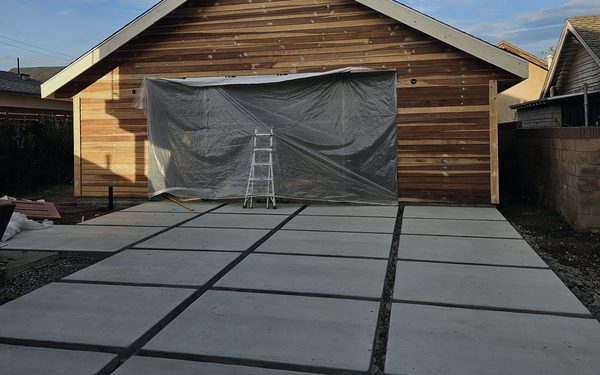 New detached garage with vertical wood siding, fronted by a concrete apron poured as separate panels with gravel joints between them