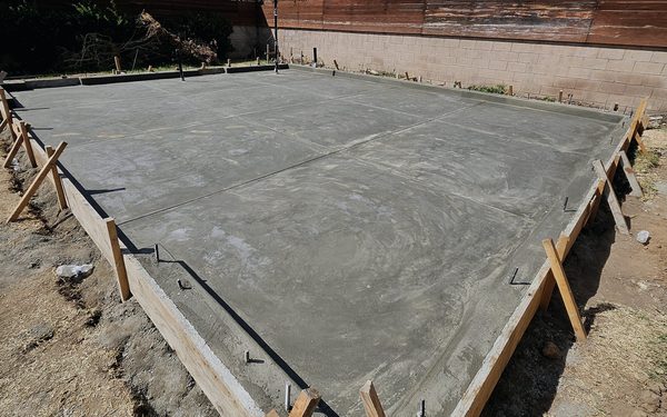 Freshly poured garage slab sitting in braced timber forms, with anchor bolts set upright around the perimeter