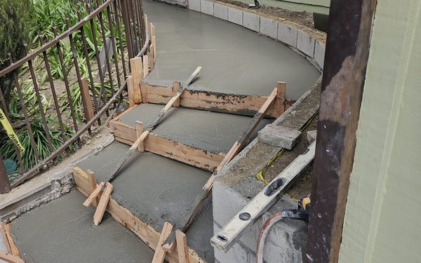 Freshly poured concrete steps and a curved walkway, still in their timber forms beside a block wall