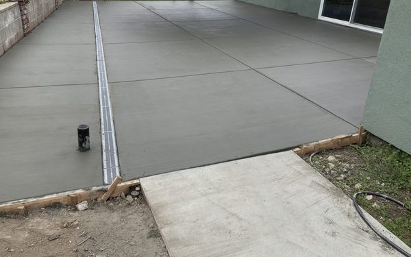 Freshly poured concrete patio with tooled joints and a stainless trench drain running along one edge, timber forms still in place