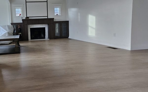 Living room with a new wide plank floor running toward a dark wood fireplace surround and built in cabinets