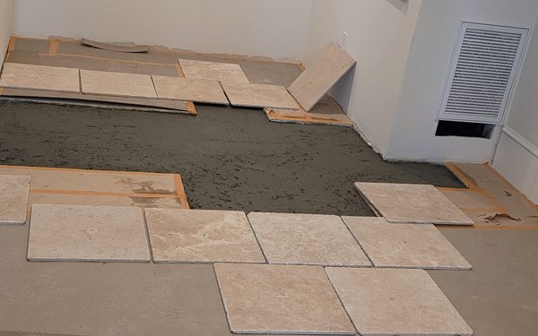 Travertine tiles being set on a fresh mortar bed, with several pieces placed and the rest of the bed still open