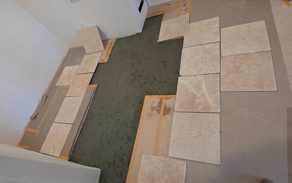 Overhead view of large travertine tiles going down on a mortar bed, laid out in a repeating pattern