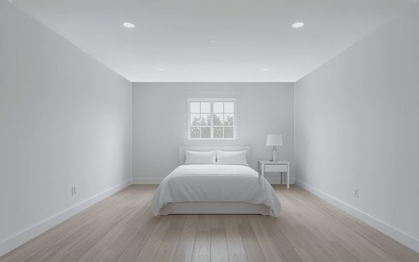 Design rendering of a long white bedroom with recessed ceiling lights, a bed with white bedding under a single window, a white nightstand with a lamp, and a pale wood look plank floor
