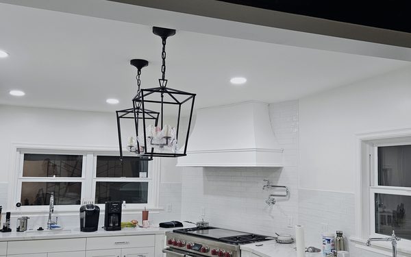 White shaker kitchen with a plaster range hood, a wall mounted pot filler above the range, subway tile, and a lantern pendant over the counter