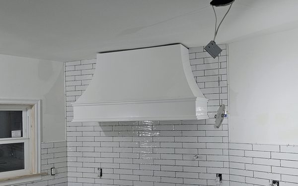 Subway tile backsplash carried full height up a range hood wall, with the hood set and the outlet boxes still open before trim