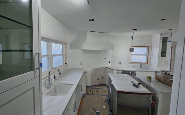 Galley kitchen part way through install, with new white cabinets and stone countertops set, a sink plumbed in, and the floor still covered