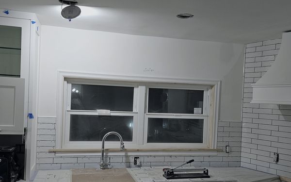 Subway tile going in around a double window over the sink, with a tile cutter on the covered counter