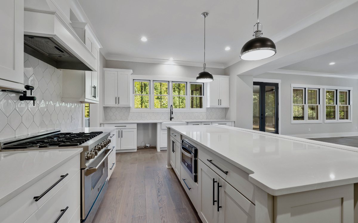 White shaker kitchen with a quartz waterfall island, pendant lights, and a professional gas range