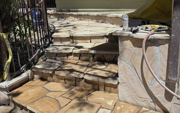 Flagstone steps and a stone faced planter part way through installation, with cut stone stacked ready to set