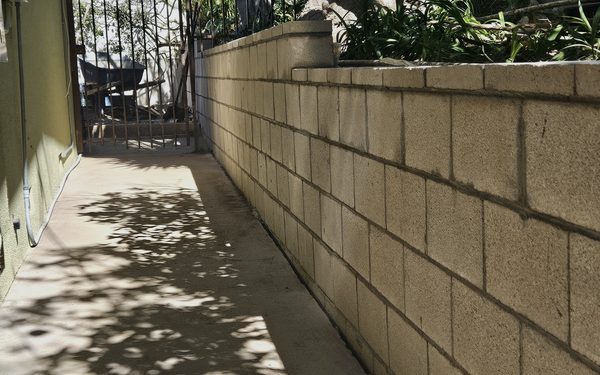 Finished block retaining wall running the length of a side yard beside a concrete path