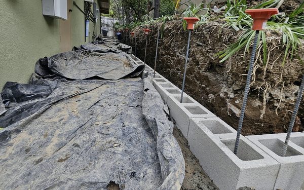 First course of a block wall laid on its footing, with vertical rebar standing up through the cells and sheeting over the ground