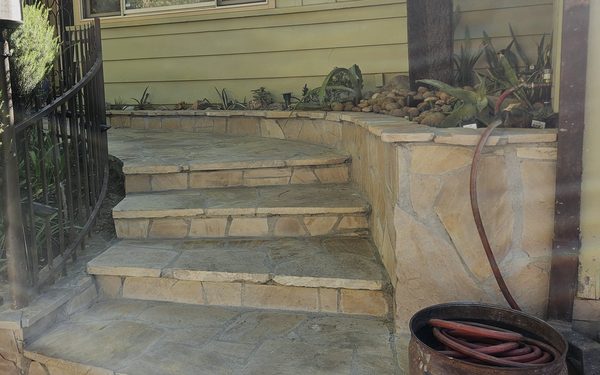 Flagstone front steps and landing with a stone faced planter wall beside them, planted with succulents