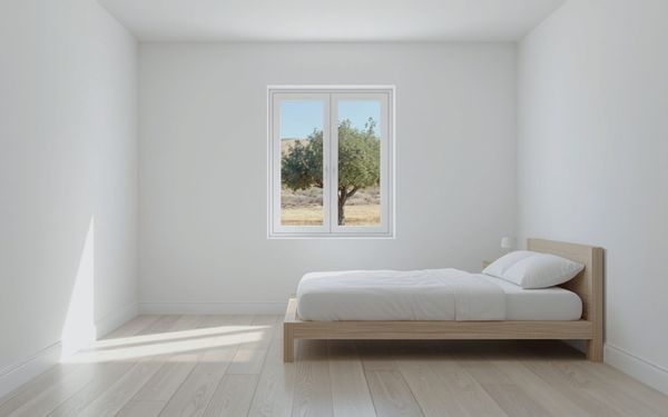 Design rendering of a plain white bedroom with a closed two sash white casement window looking out on an olive tree and dry hills, a light wood platform bed with white bedding, and a light wood look plank floor